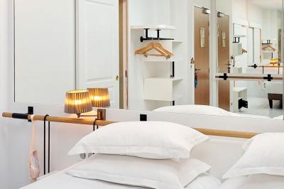 Lit avec oreillers blancs, lampe de chevet allumée et miroir reflétant une penderie et des portes dans une chambre lumineuse.