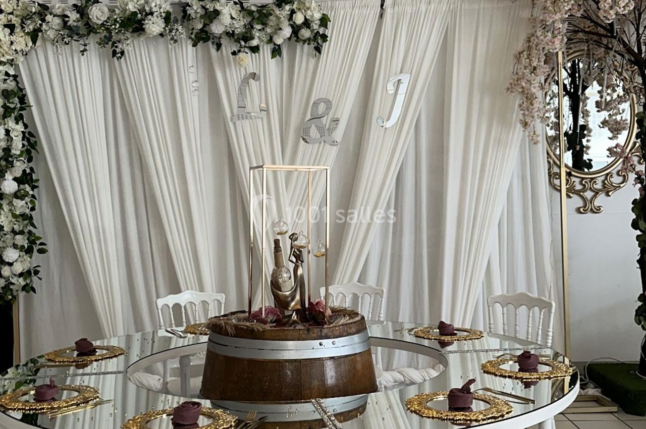 Table décorée pour un événement, avec nappes blanches, chaises assorties, centre de table floral et assiettes dorées.
