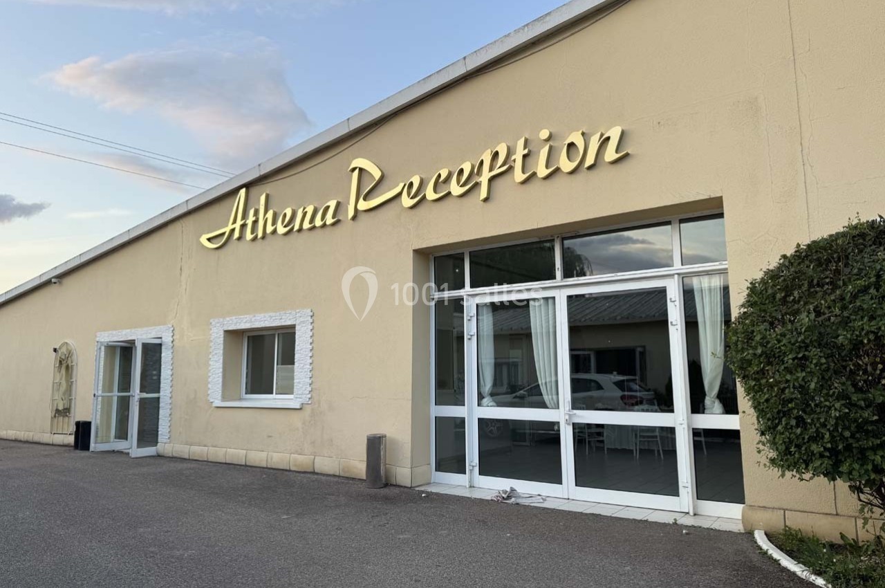 Façade d'un bâtiment beige avec l'inscription lumineuse ’Athena Reception’ au-dessus de l'entrée vitrée.