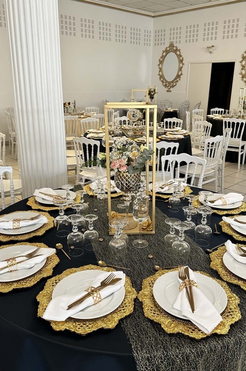 Table élégamment dressée avec des assiettes blanches, des serviettes pliées et des décorations dorées dans une salle de…