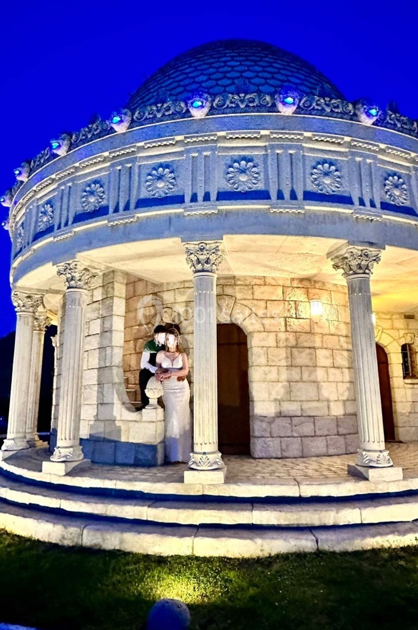 Petit pavillon en pierre avec colonnes et dôme illuminé, photographié de nuit sous un ciel bleu profond.