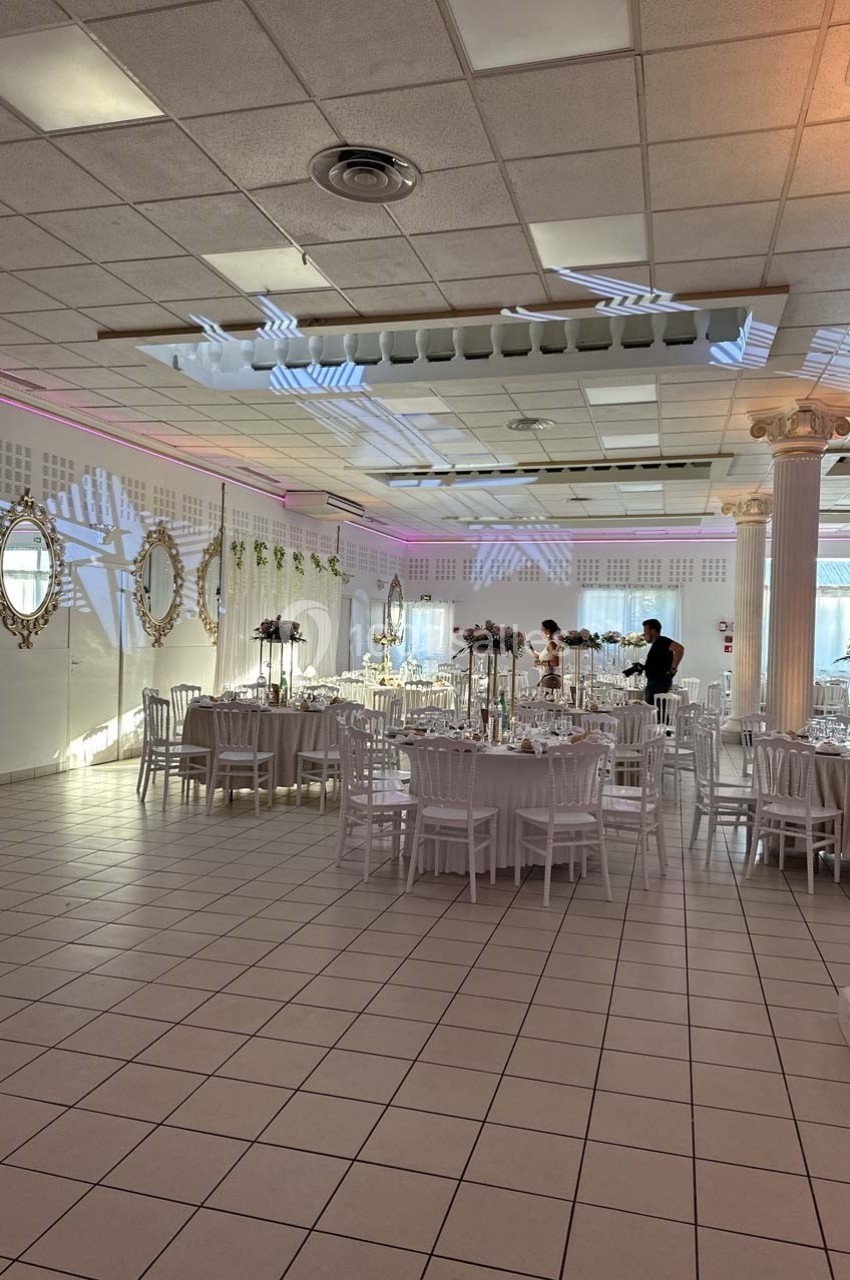 Salle de réception lumineuse avec tables décorées, chaises blanches et miroirs ornant les murs.
