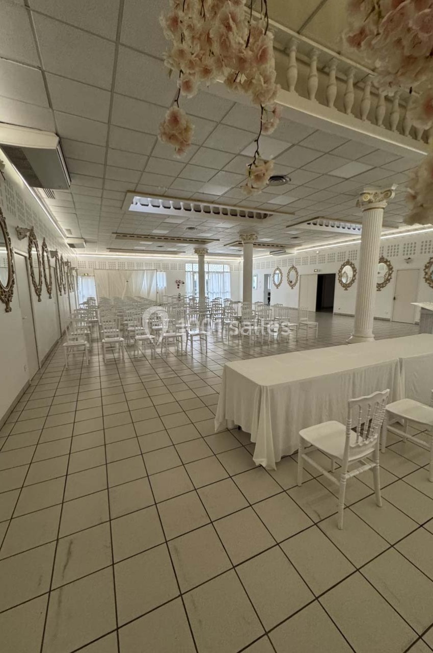 Salle de réception lumineuse avec tables et chaises blanches, décorée de colonnes et de miroirs muraux.