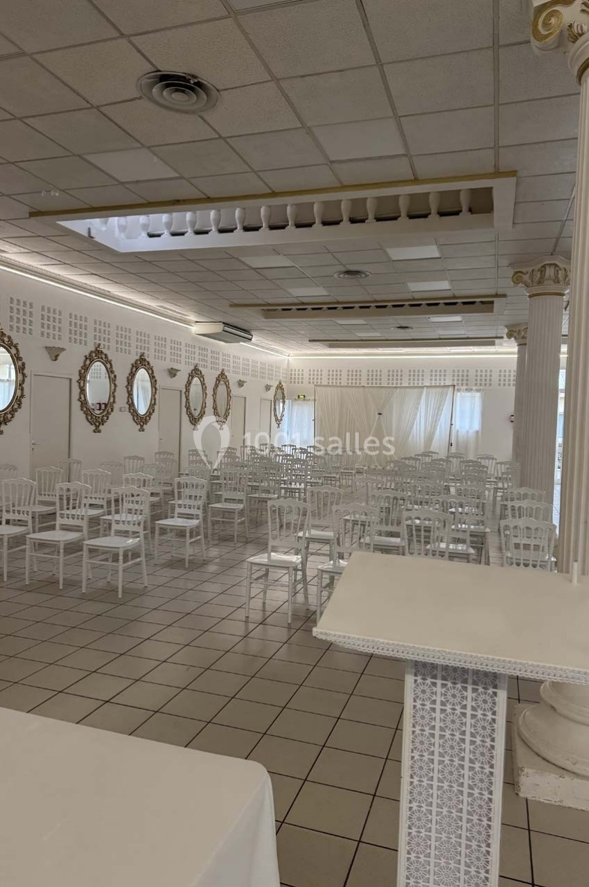 Salle de réception lumineuse avec des chaises blanches alignées, des miroirs dorés et des colonnes décoratives.