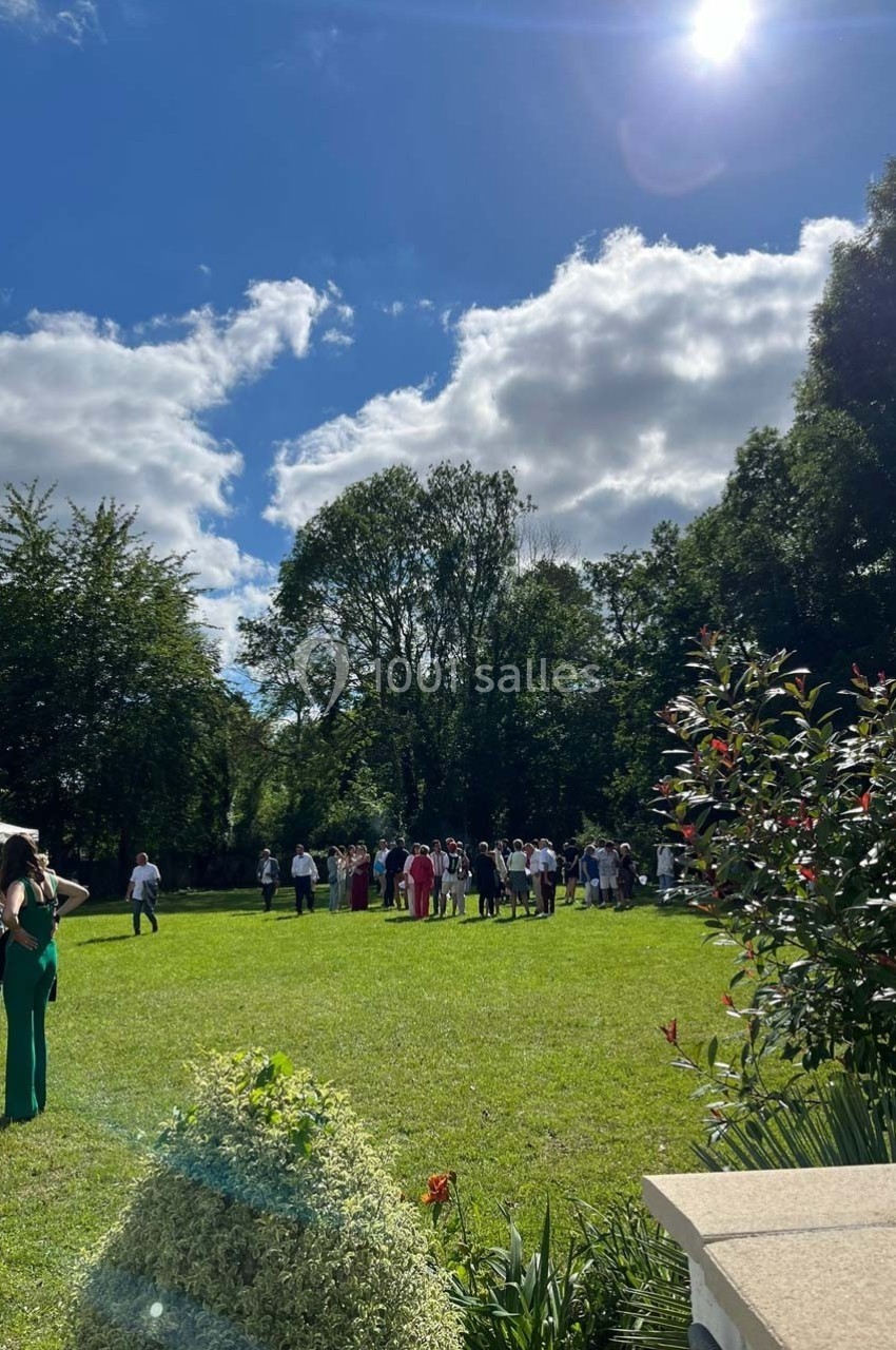 Groupe de personnes rassemblées dans un jardin ensoleillé, entouré d'arbres et de végétation.