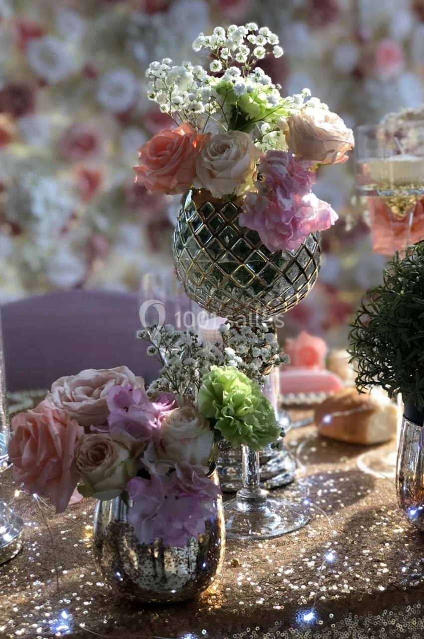 Arrangements floraux avec roses, hortensias et gypsophiles dans des vases décoratifs sur une table scintillante.
