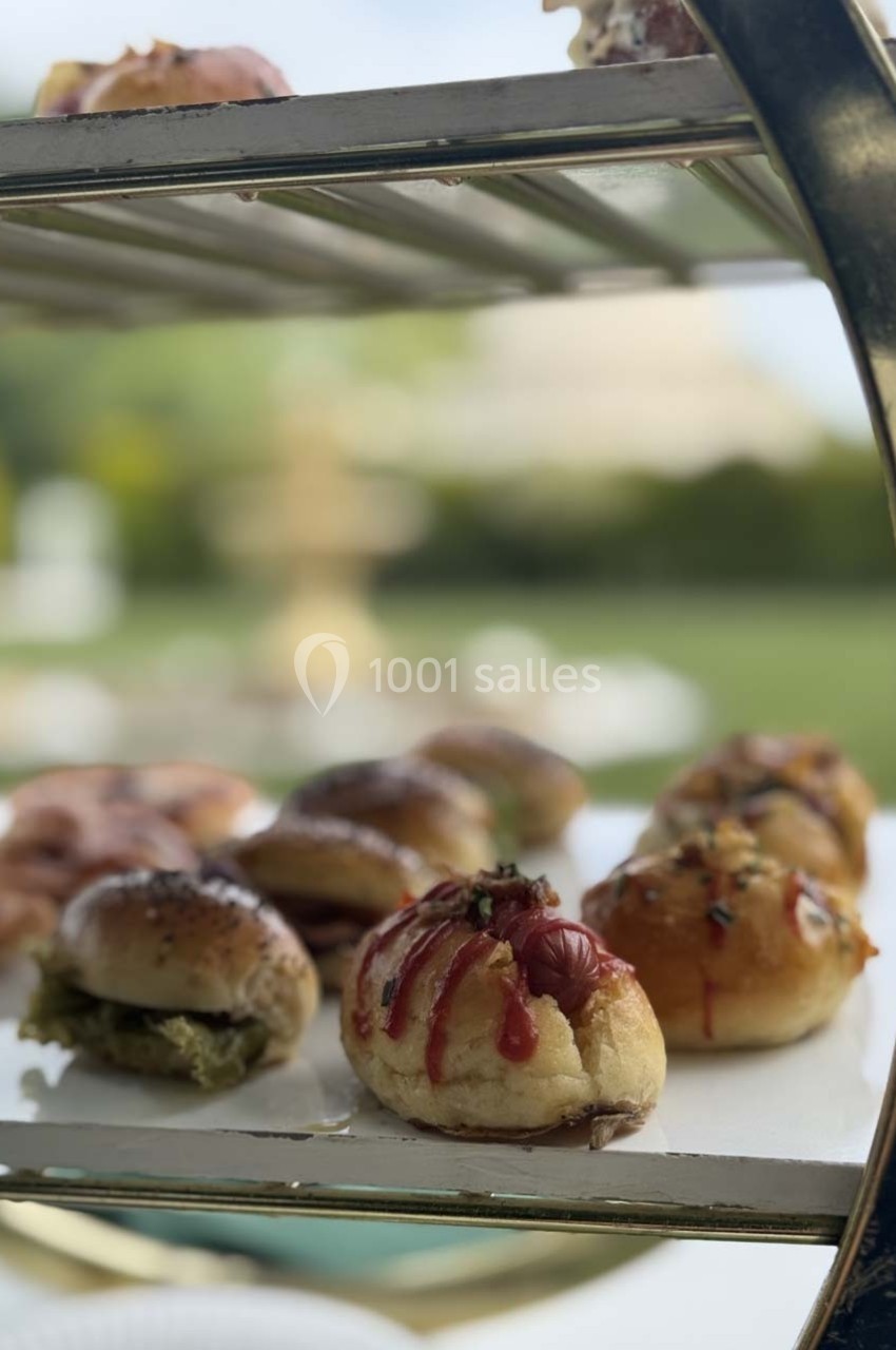 Plateau de petits pains garnis, présentés sur une étagère métallique avec un jardin flou en arrière-plan.