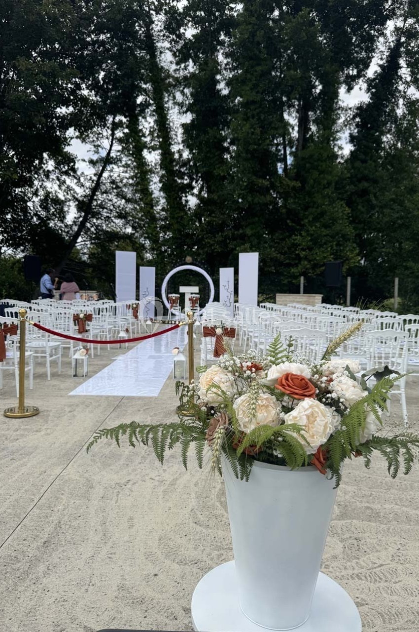 Allée décorée pour une cérémonie en extérieur avec des chaises blanches, un tapis blanc et des fleurs en premier plan.