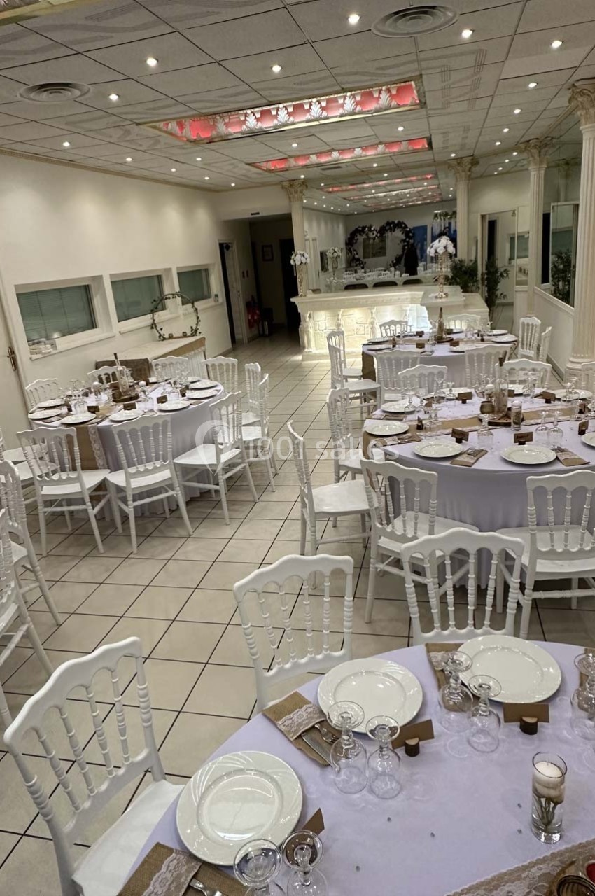 Salle de réception décorée avec des tables rondes dressées, nappes blanches et chaises assorties, éclairage lumineux.