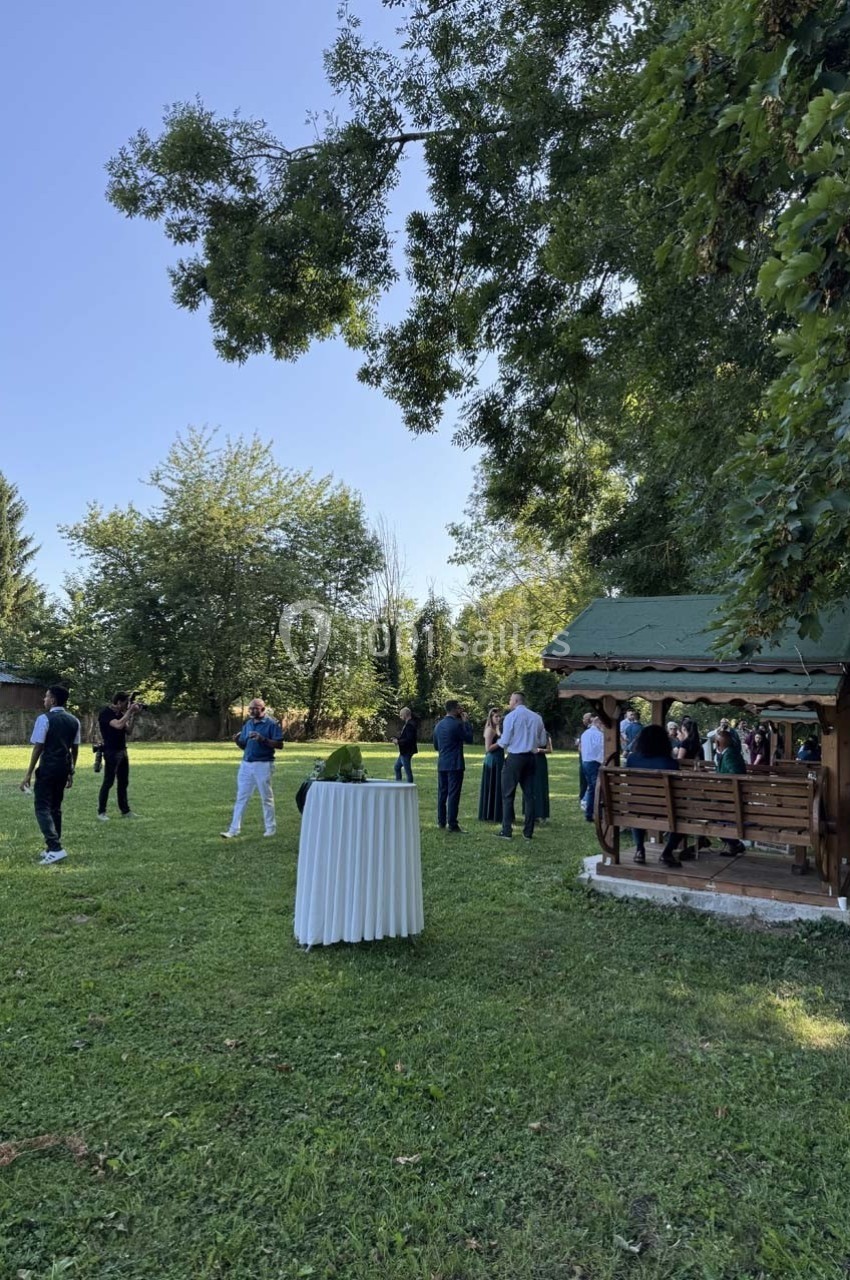 Un groupe de personnes discutant dans un jardin verdoyant avec une tonnelle en bois et une table haute en premier plan.