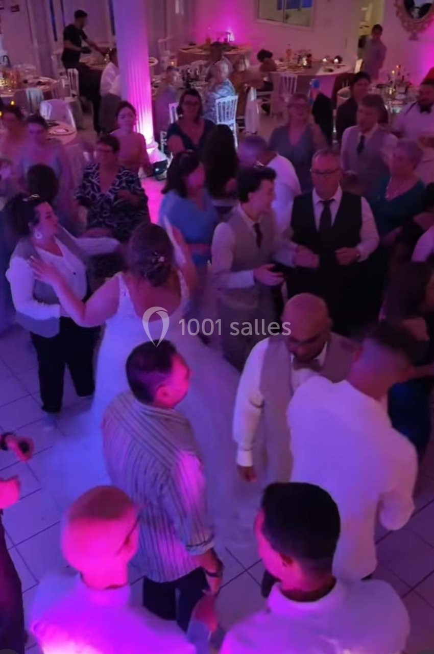 Groupe de personnes dansant lors d'une réception festive dans une salle éclairée par des lumières colorées.