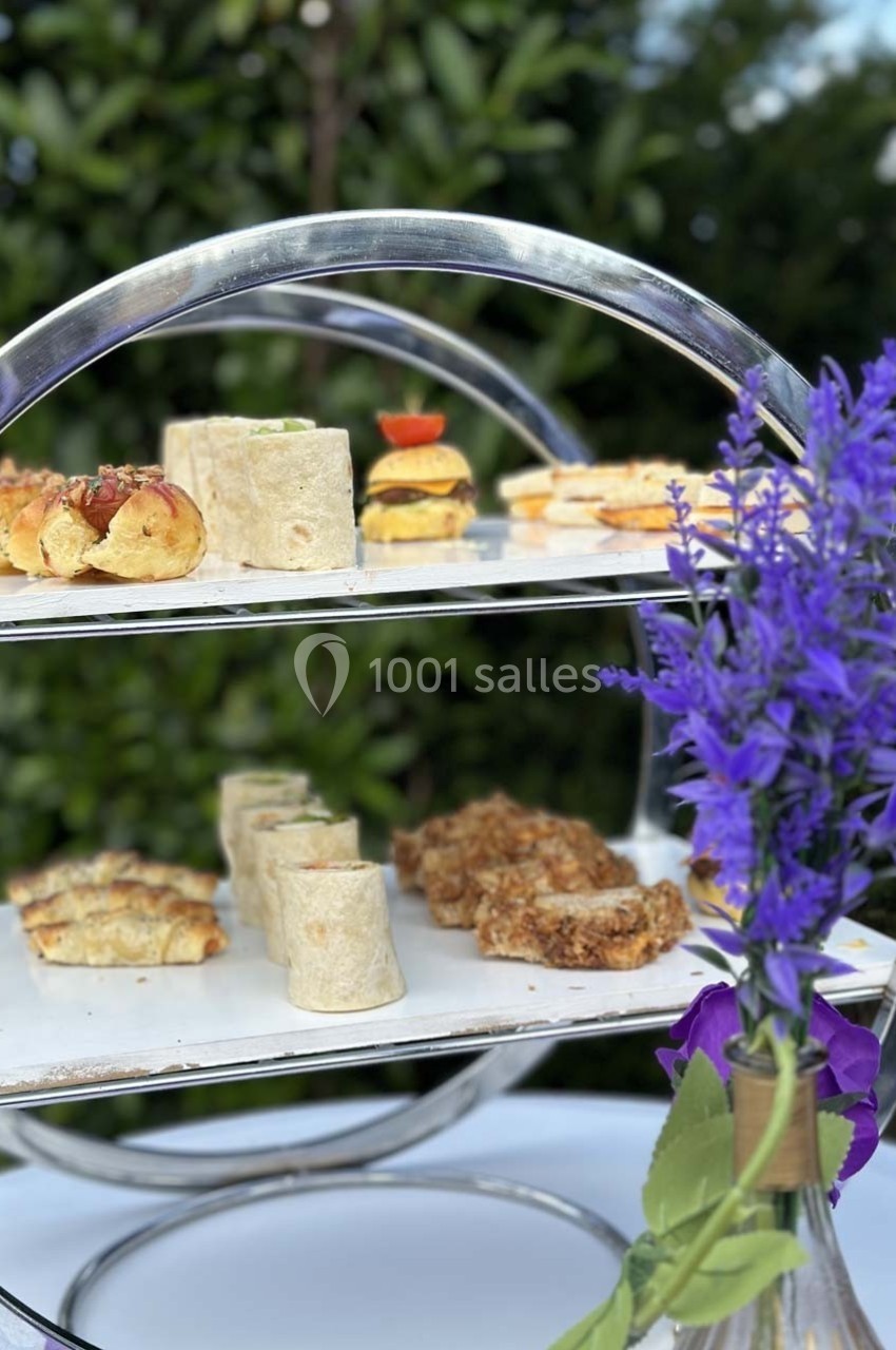 Plateau à étages avec des amuse-bouches variés, accompagné d'un bouquet de fleurs violettes au premier plan.
