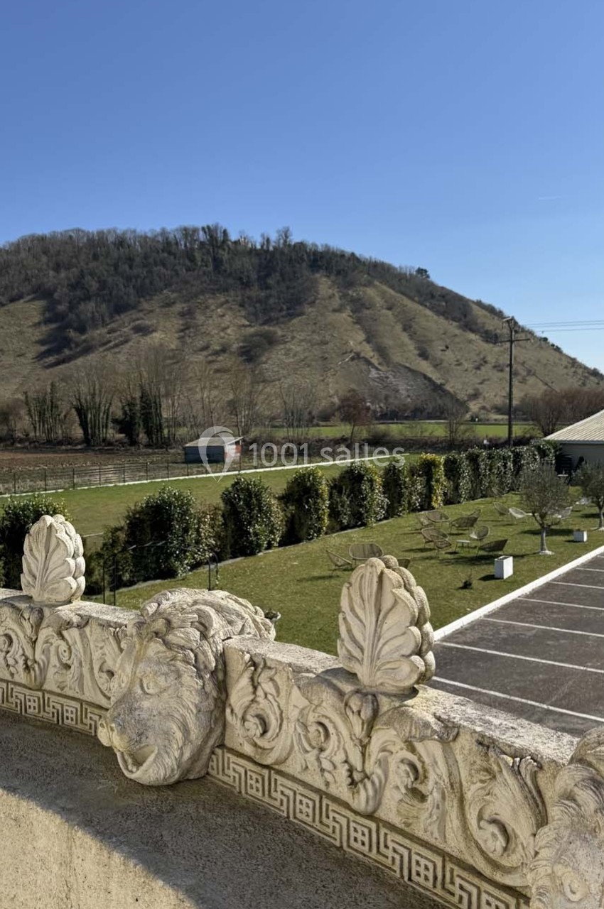 Vue d'une colline verdoyante sous un ciel bleu, avec un premier plan de balustrade ornée de sculptures.