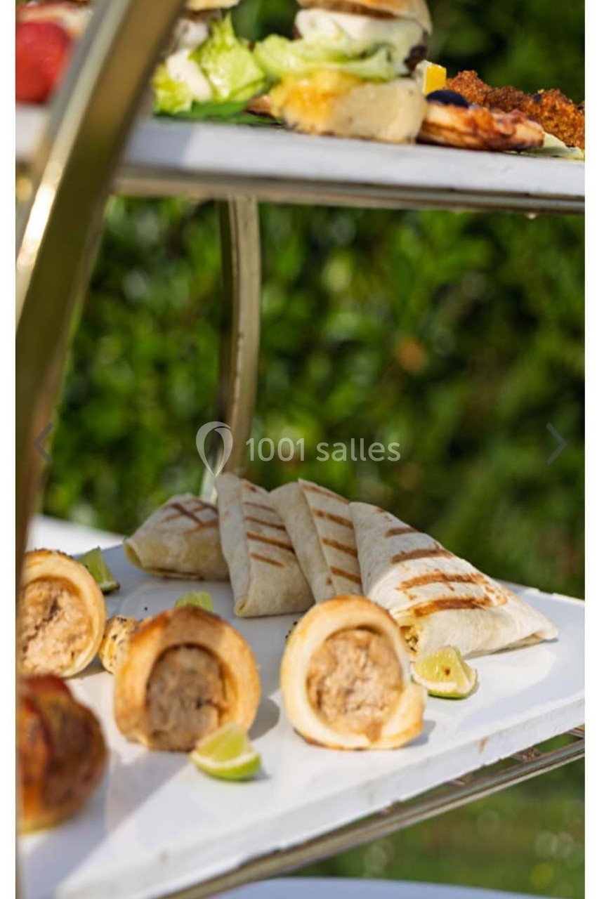 Plateau de service avec wraps grillés, feuilletés farcis et mini-burgers, disposés sur deux étages en extérieur.