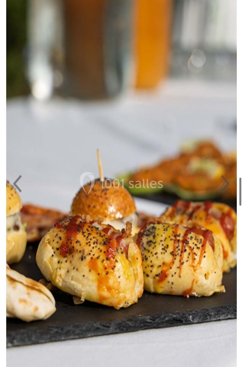 Assortiment de petits pains garnis et saupoudrés de graines, présentés sur une ardoise lors d'un repas en extérieur.
