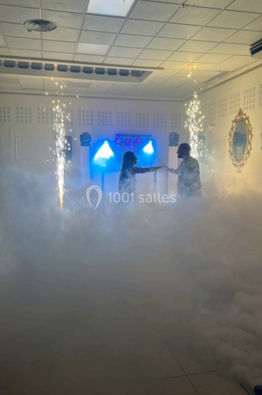 Deux personnes dansent au milieu de la fumée et d'effets lumineux avec des étincelles dans une salle fermée.