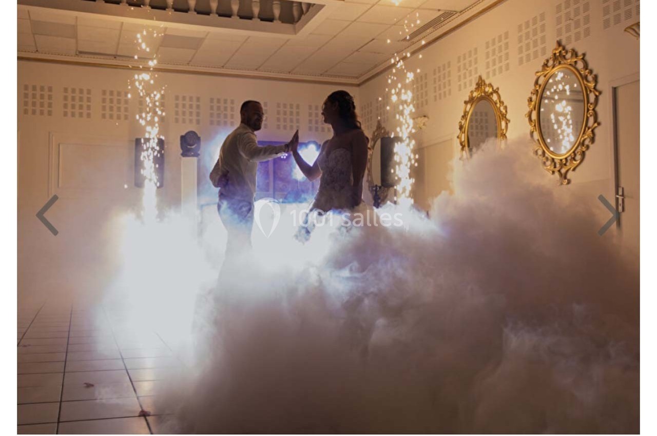 Un couple danse au milieu de fumée et d'effets pyrotechniques dans une salle décorée avec des miroirs dorés.