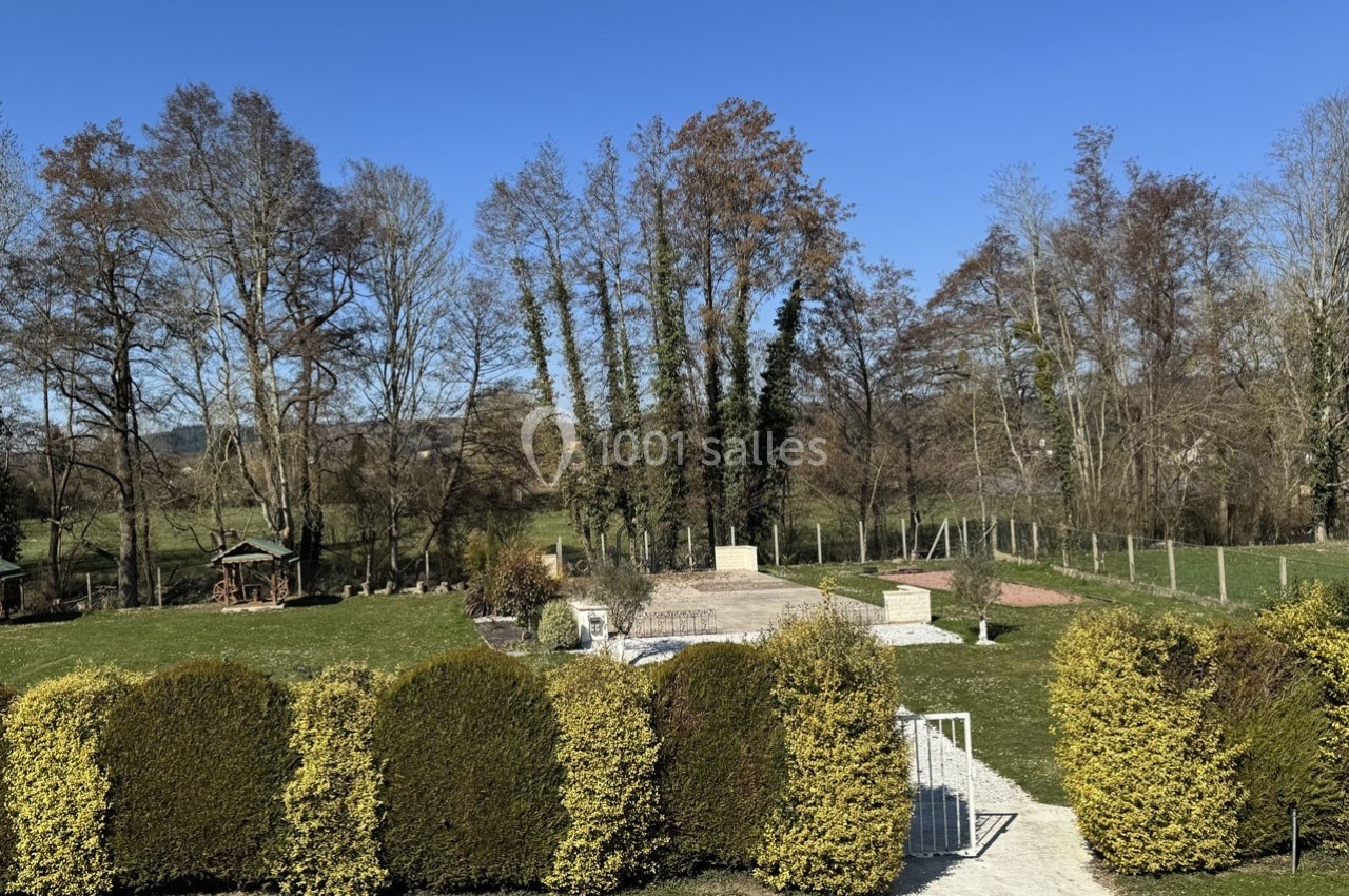 Vue d'un jardin arboré avec pelouse, haies taillées, allée en gravier et arbres en arrière-plan sous un ciel bleu.