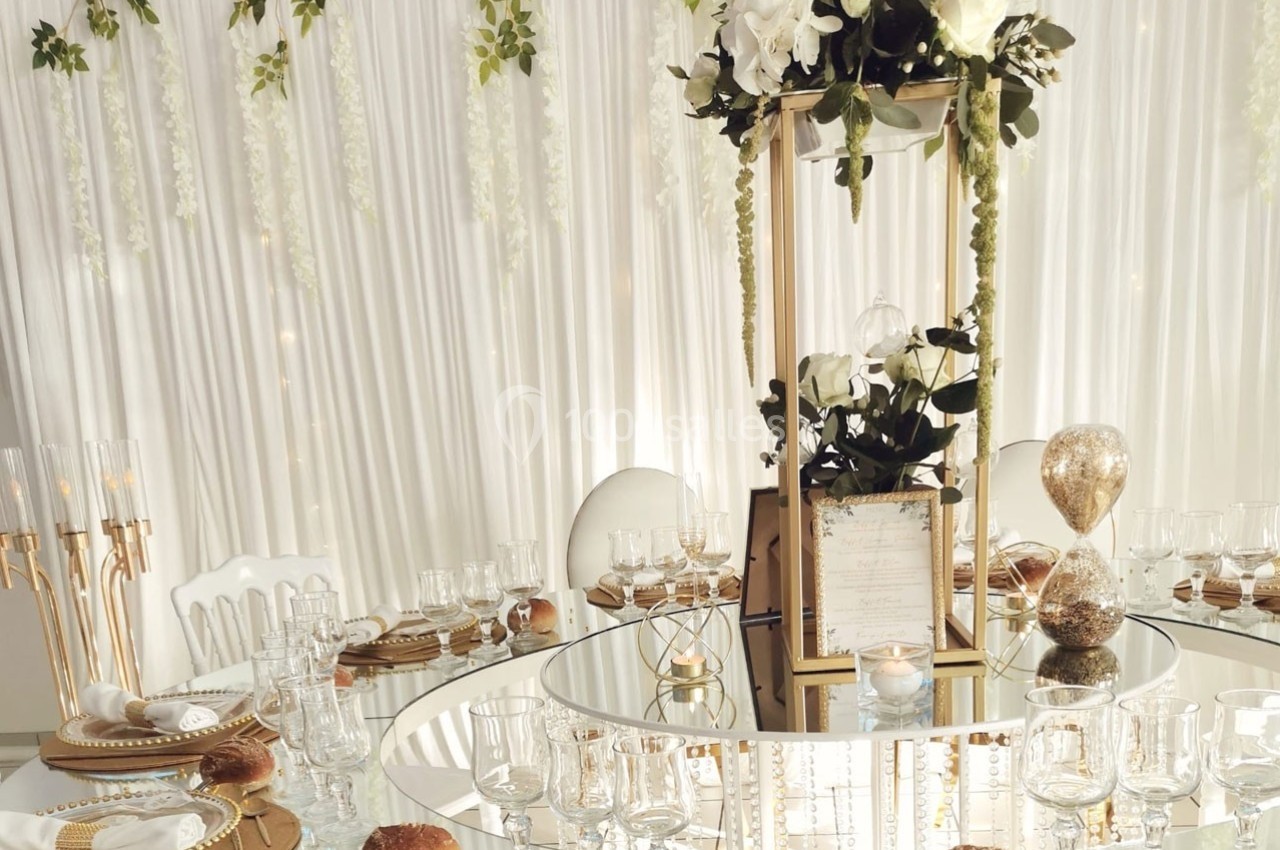 Table élégamment dressée avec vaisselle raffinée, centre de table floral et décoration lumineuse en arrière-plan.