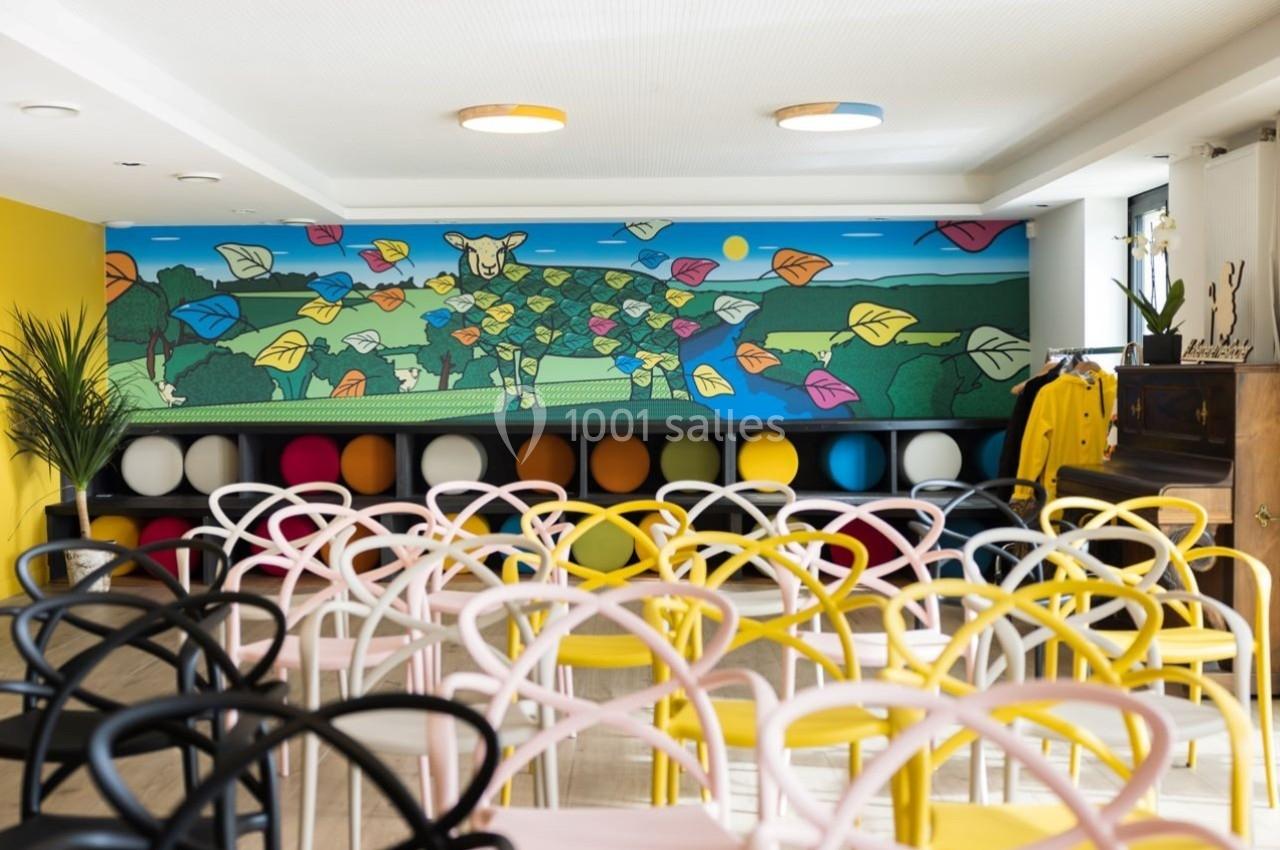Salle colorée avec des chaises design, un mur décoré d'une fresque vive représentant une vache et des feuilles.