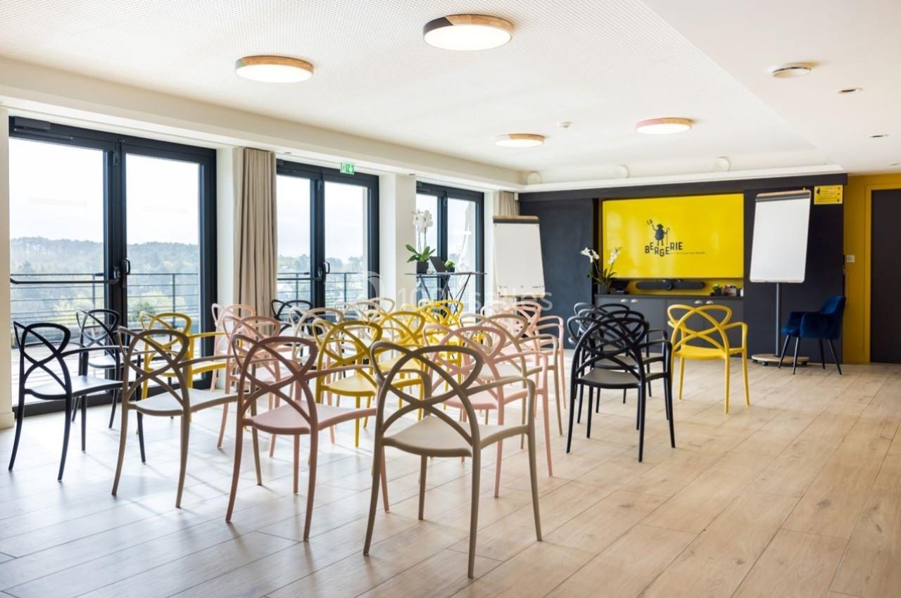 Salle de réunion lumineuse avec des chaises colorées, des tableaux de présentation et une vue extérieure dégagée.