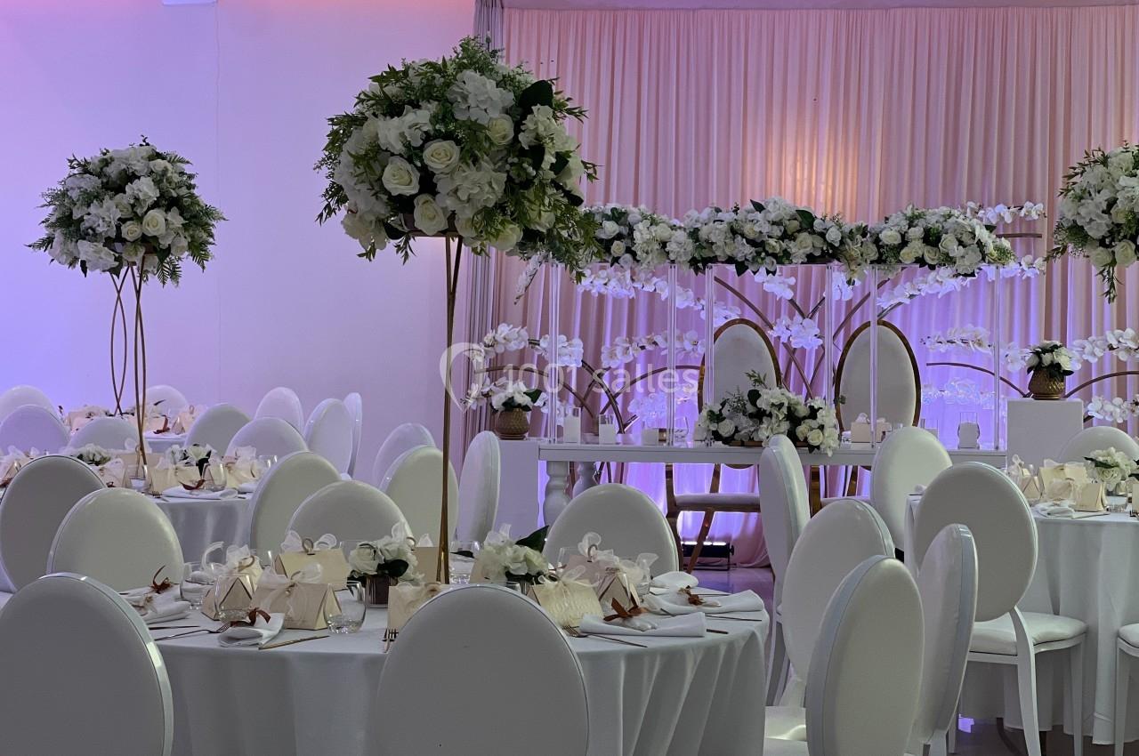 Salle de réception décorée avec des tables rondes, des chaises blanches et des arrangements floraux élégants.
