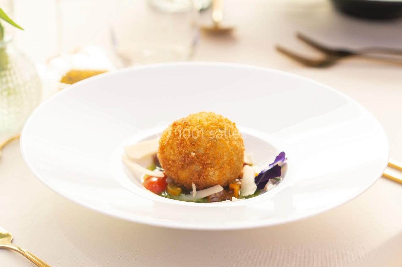 Croquette dorée servie sur un lit de légumes colorés et décorée de pétales de fleurs dans une assiette blanche.