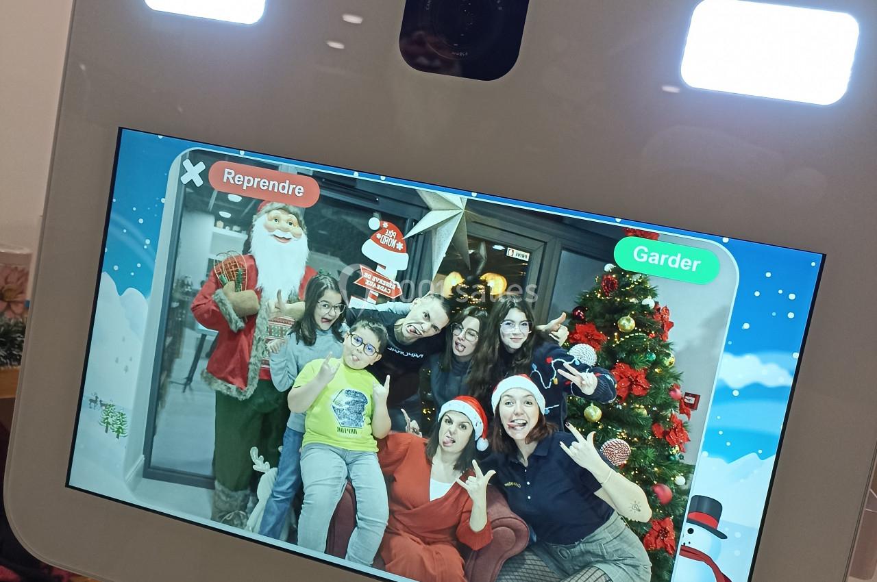 Des personnes souriantes posent devant un écran de photobooth avec des décorations de Noël en arrière-plan.