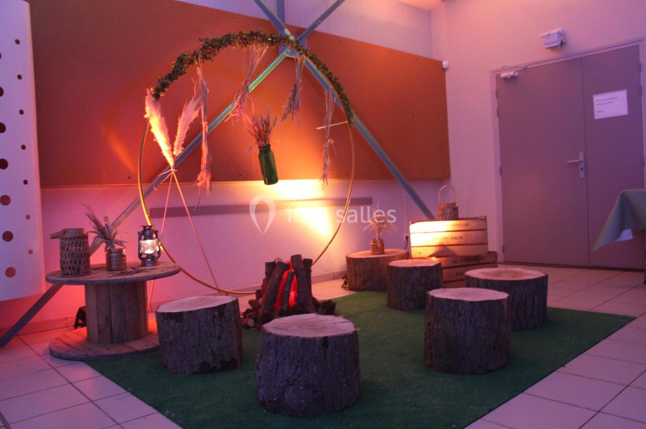 Espace décoratif intérieur avec rondins de bois en sièges, feu artificiel, et éléments naturels suspendus.