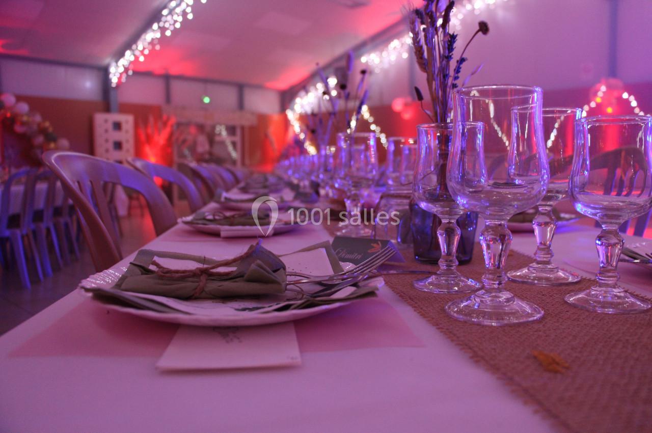 Table décorée pour un événement, avec nappes blanches, verres, couverts et éclairage tamisé aux tons roses.