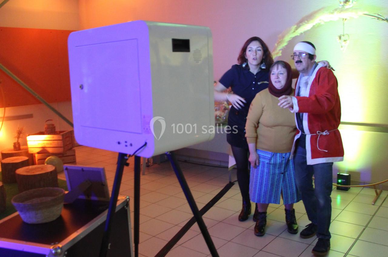 Trois personnes interagissent avec une borne photo dans une pièce éclairée par des lumières colorées.