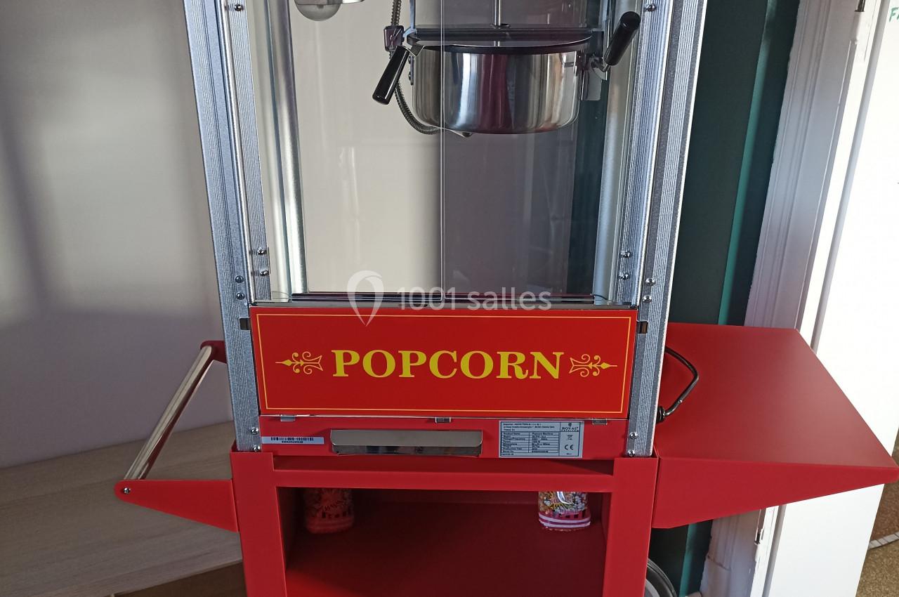 Machine à popcorn rouge sur roulettes, avec compartiment de rangement et inscription ’Hot & Fresh’ sur le haut.
