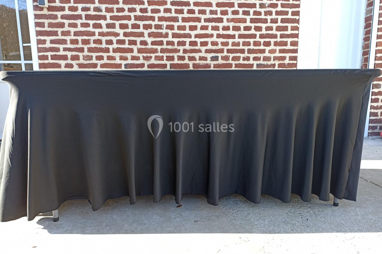 Table recouverte d'une nappe noire plissée, placée devant un mur de briques rouges et une porte blanche.