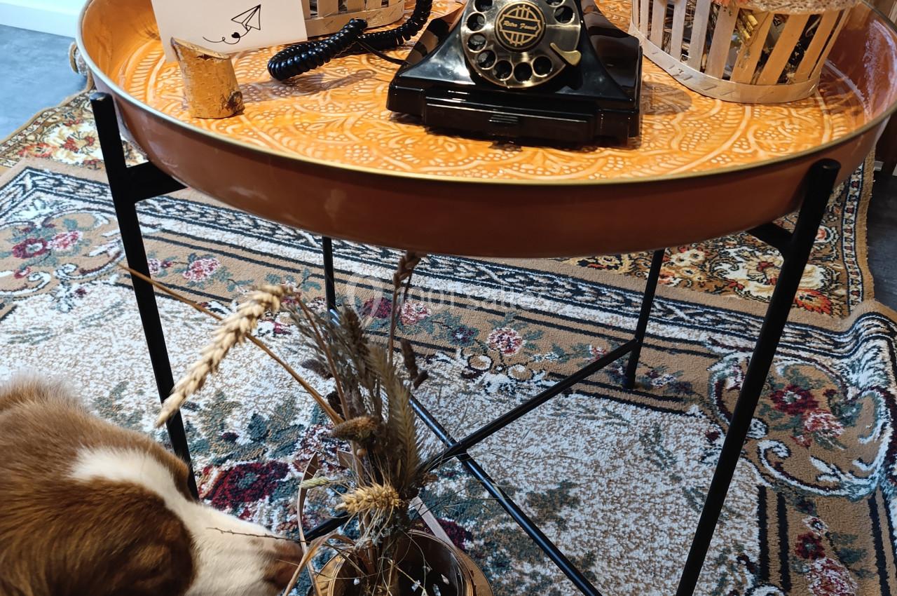 Un téléphone vintage noir posé sur une table ronde orange, entouré de décorations en fleurs séchées.
