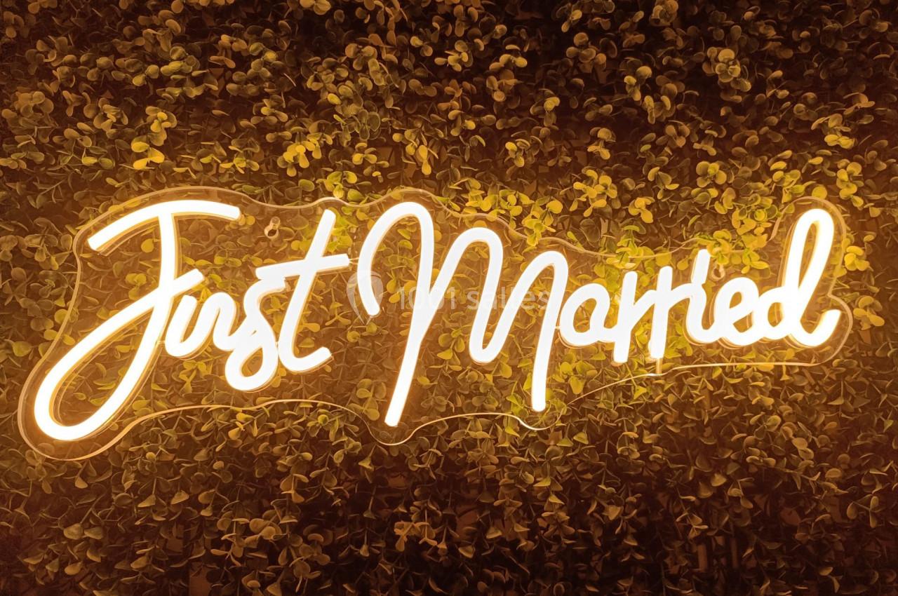 Texte lumineux ’Just Married’ sur un mur végétal sombre.