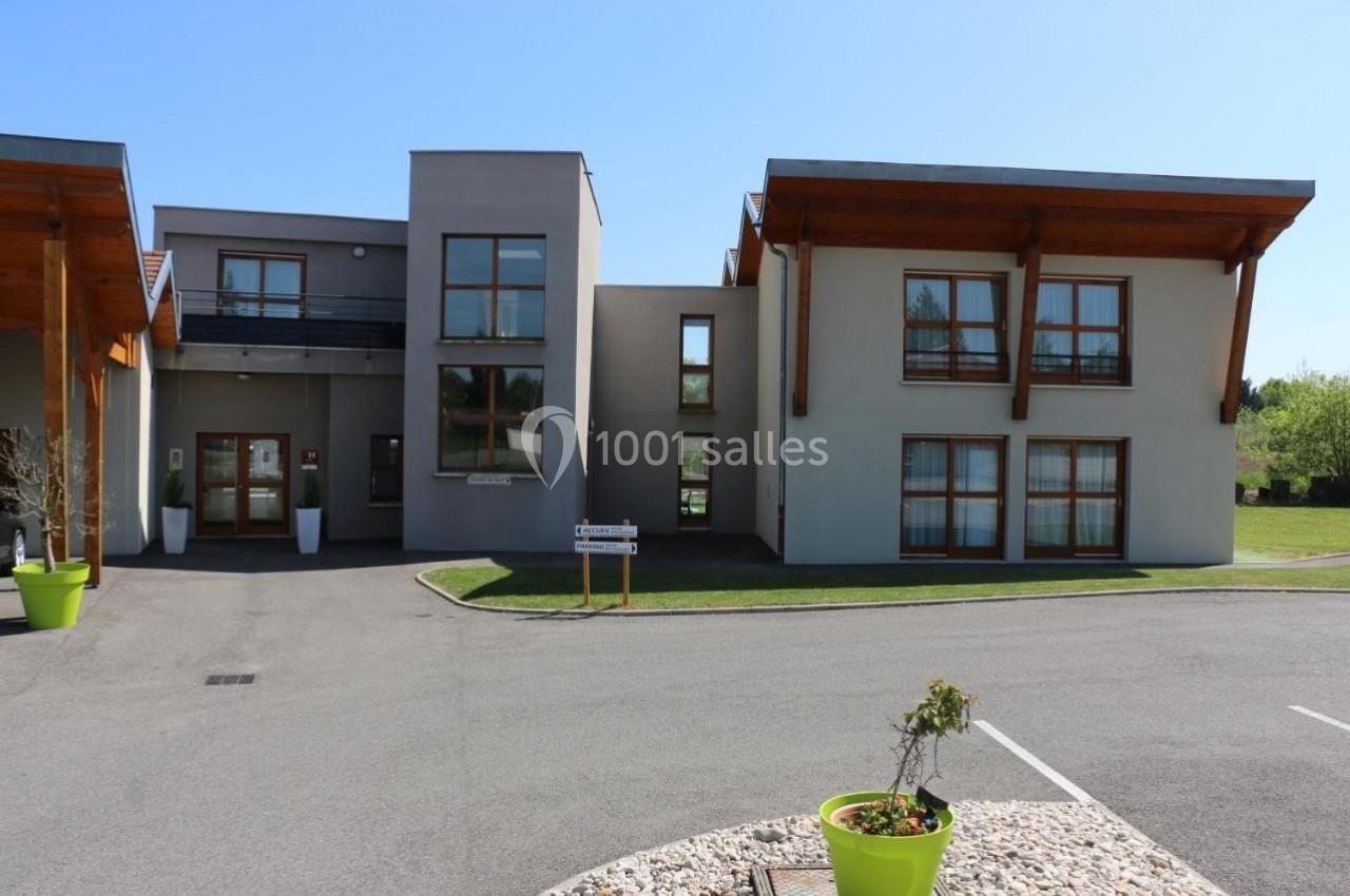 Bâtiment moderne à deux étages avec grandes fenêtres, entouré d'une allée et d'espaces verts.