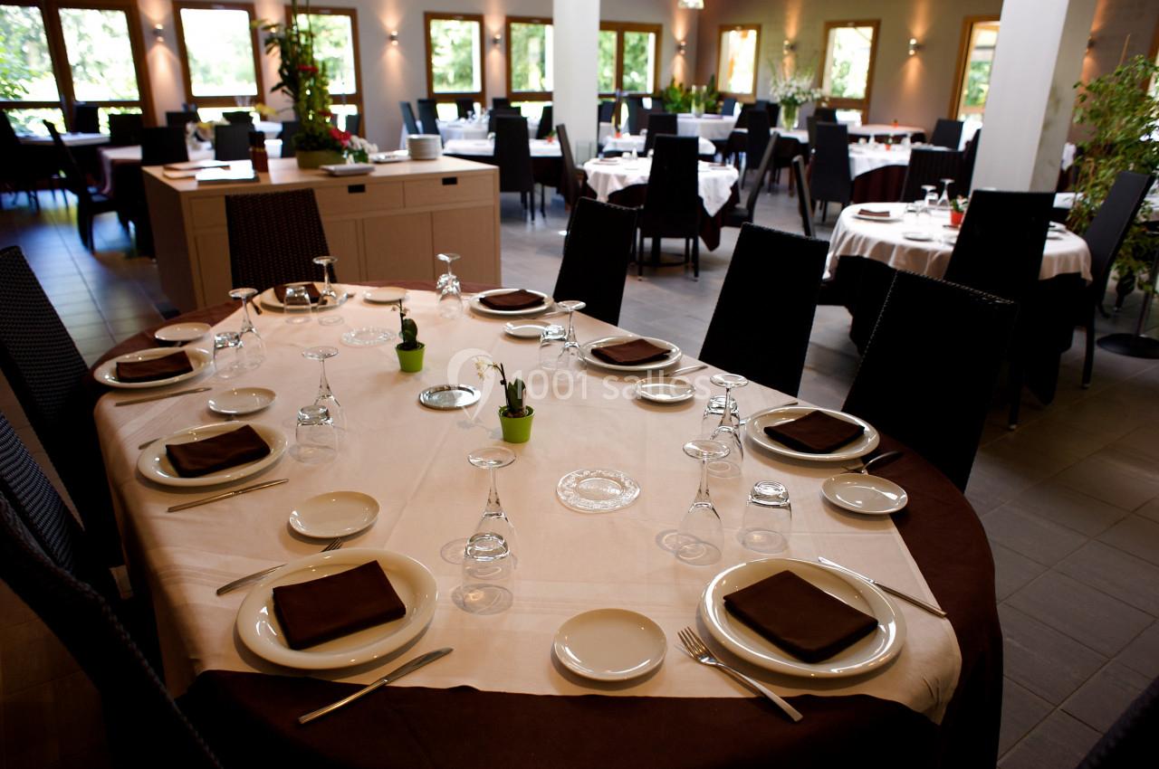 Salle de restaurant élégante avec tables dressées, nappes blanches, vaisselle et serviettes sombres, entourées de chaises…