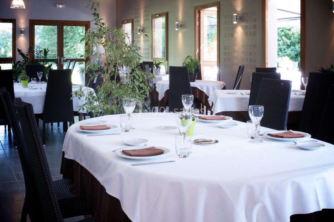 Salle de restaurant lumineuse avec tables dressées, nappes blanches, chaises noires et plantes décoratives.