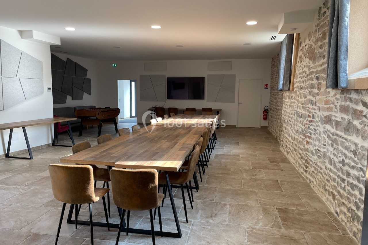 Salle lumineuse avec longues tables en bois, chaises en cuir, murs en pierre et panneaux acoustiques modernes.