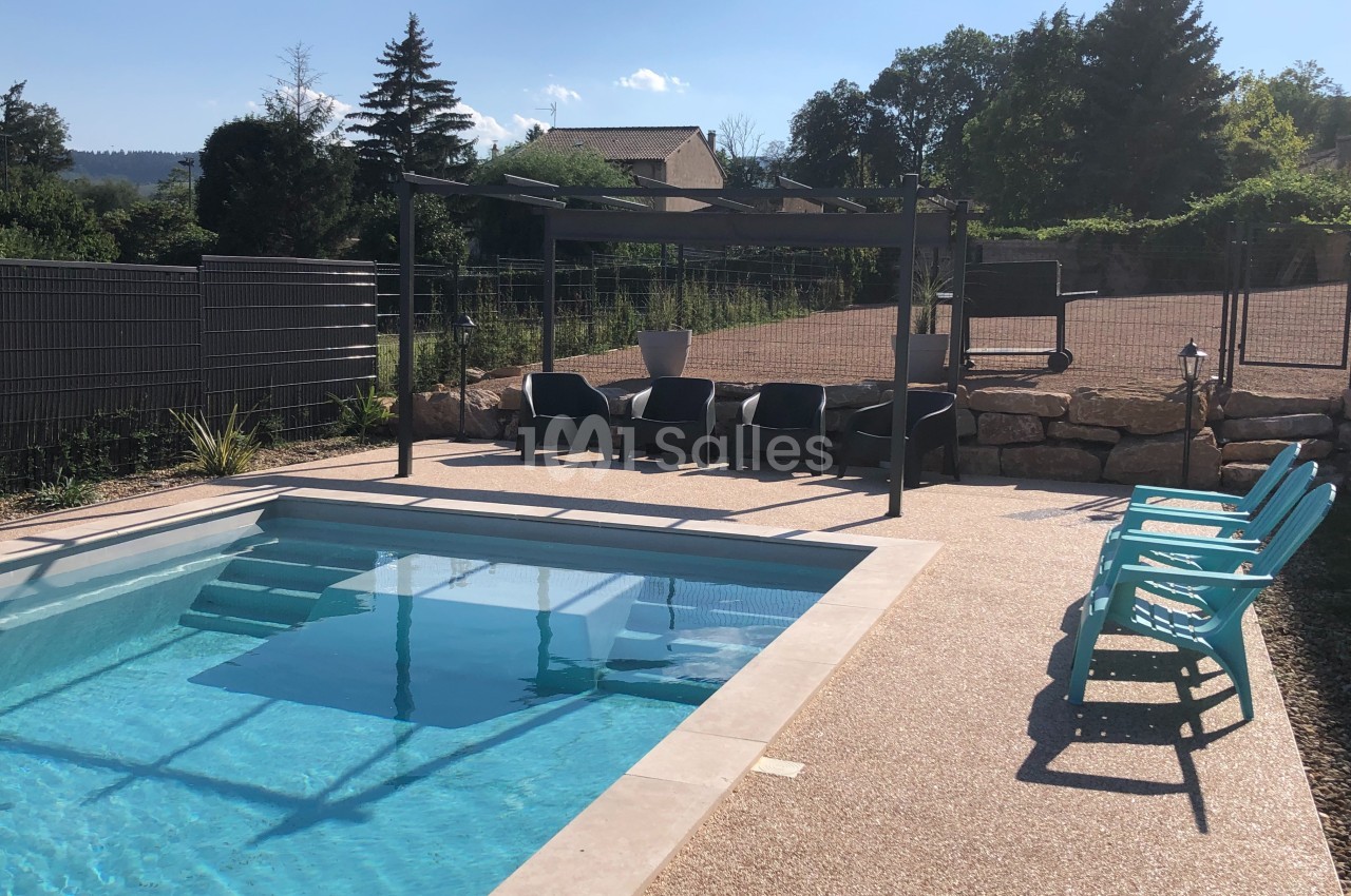 Piscine extérieure avec terrasse en gravier, chaises longues turquoise et pergola ombragée avec table et chaises.