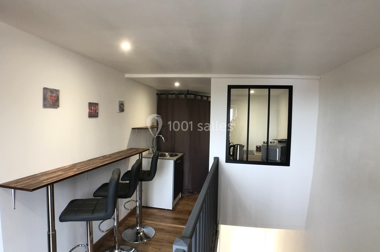 Espace intérieur avec un coin kitchenette, un bar avec tabourets hauts, et une cloison vitrée donnant sur une autre pièce.