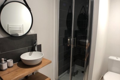 Miniature Location salle Émeringes (Rhône) - Le Cuvage By Raisin Rose #12 Salle de bain moderne avec douche vitrée, lavabo sur plan en bois, miroir rond et toilettes blanches.