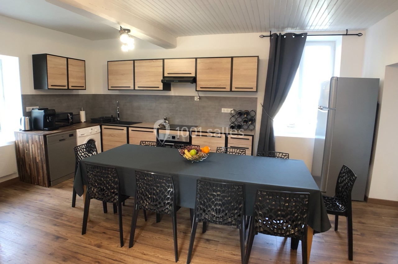 Cuisine moderne avec table rectangulaire, chaises noires ajourées, meubles en bois clair et électroménagers intégrés.