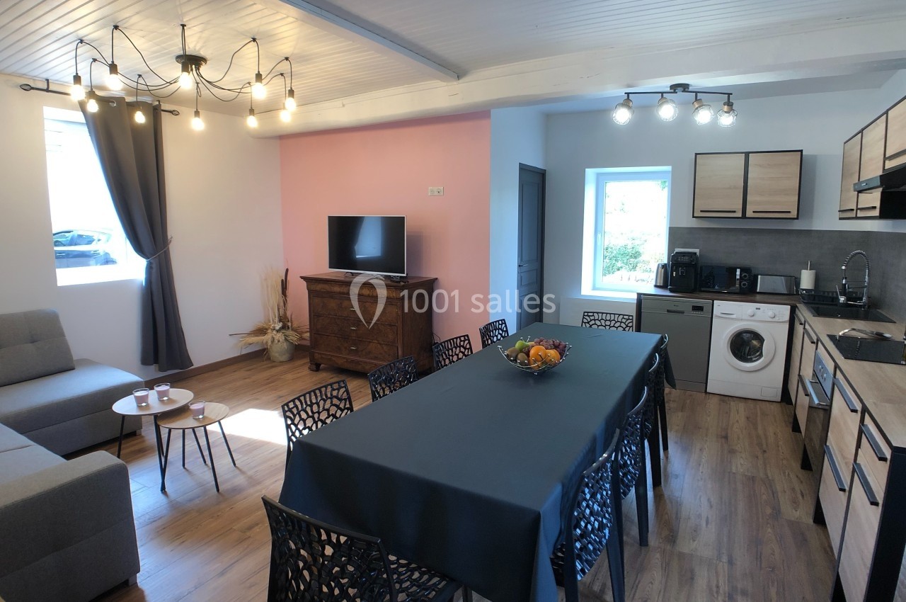 Salle à manger et salon ouverts avec table dressée, canapé, télévision, cuisine équipée et lumière naturelle.