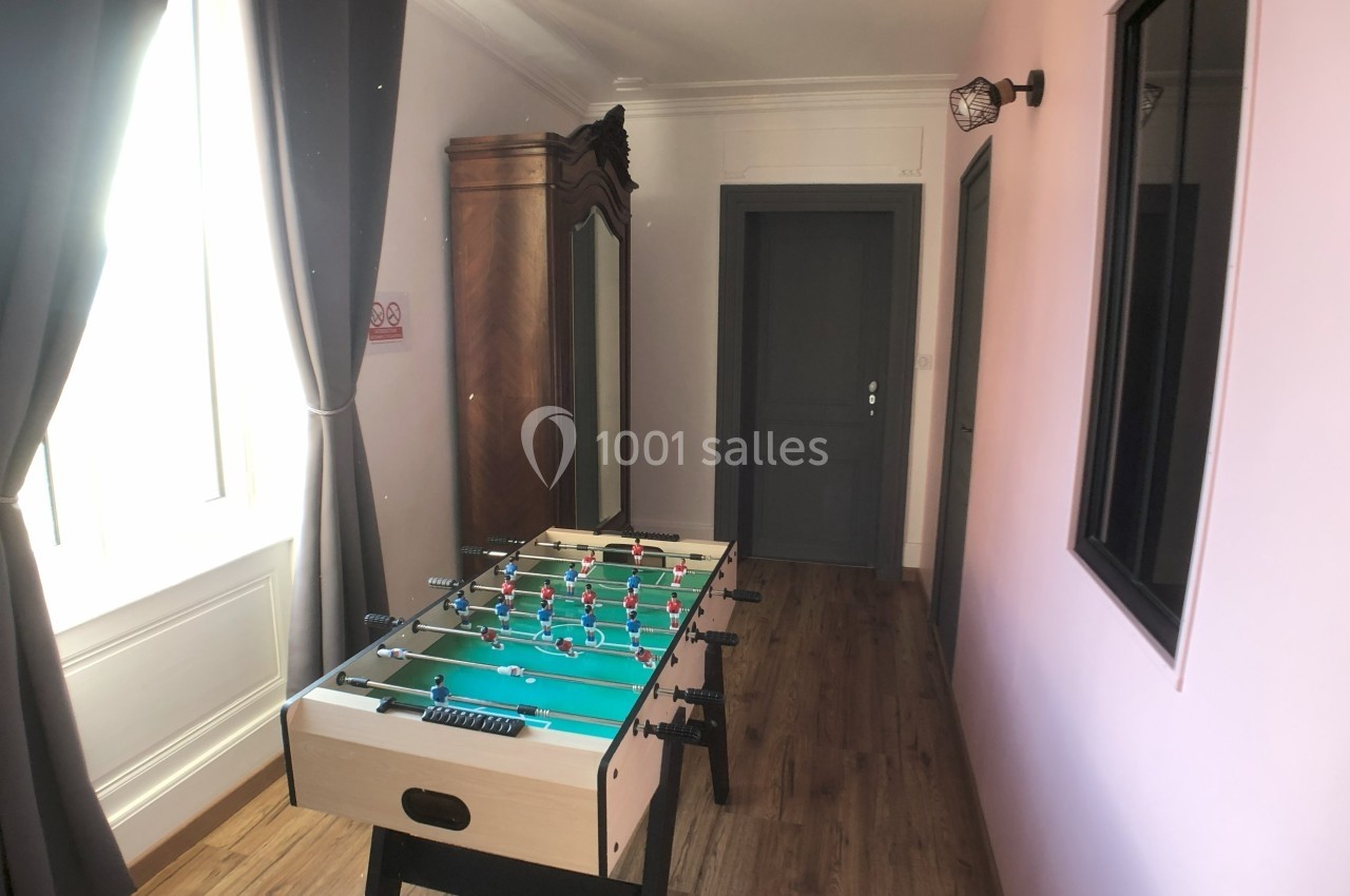 Table de baby-foot dans une pièce lumineuse avec parquet, murs roses et un grand miroir en bois.
