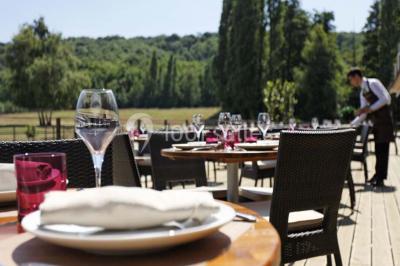 Vue aérienne d'un grand bâtiment avec toit en pente, entouré de verdure et de champs, avec un jardin aménagé au premier plan.