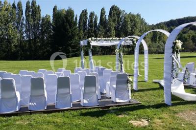 Vue aérienne d'un grand bâtiment avec toit en pente, entouré de verdure et de champs, avec un jardin aménagé au premier plan.