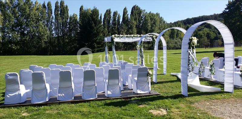 Chaises blanches alignées et arche décorée de fleurs pour une cérémonie en plein air sur une pelouse.