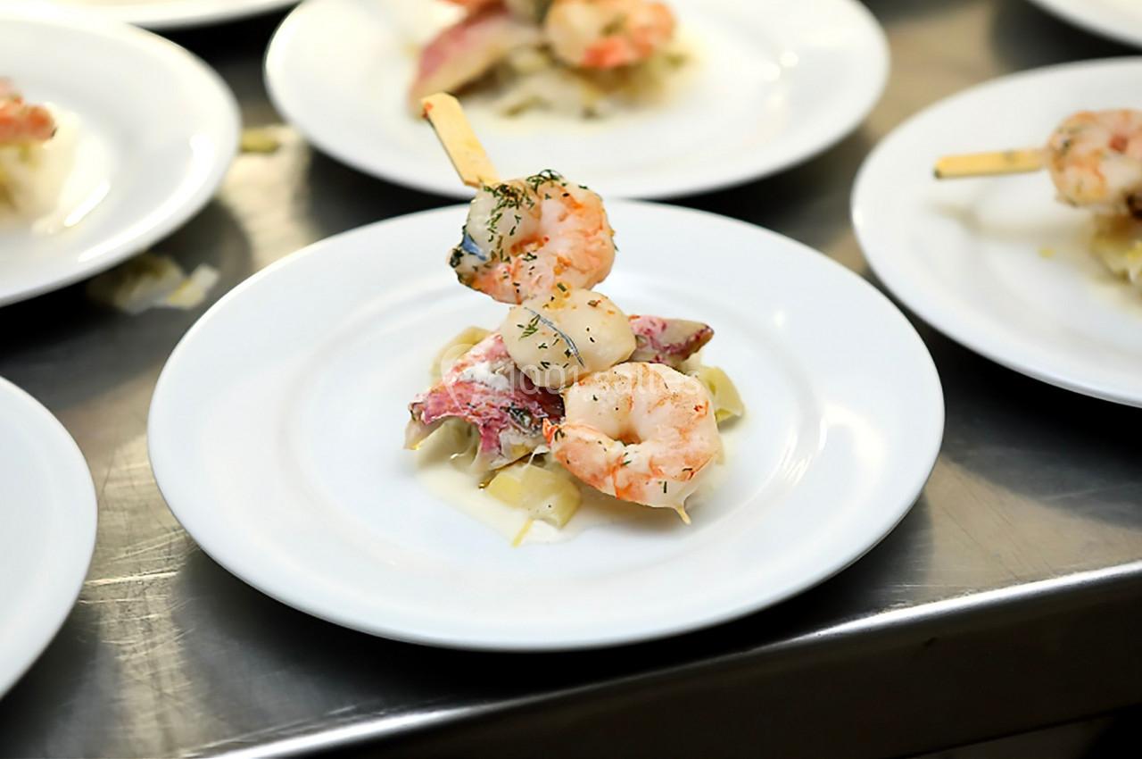 Brochette de crevettes et poisson sur un lit de légumes, servie dans une assiette blanche.