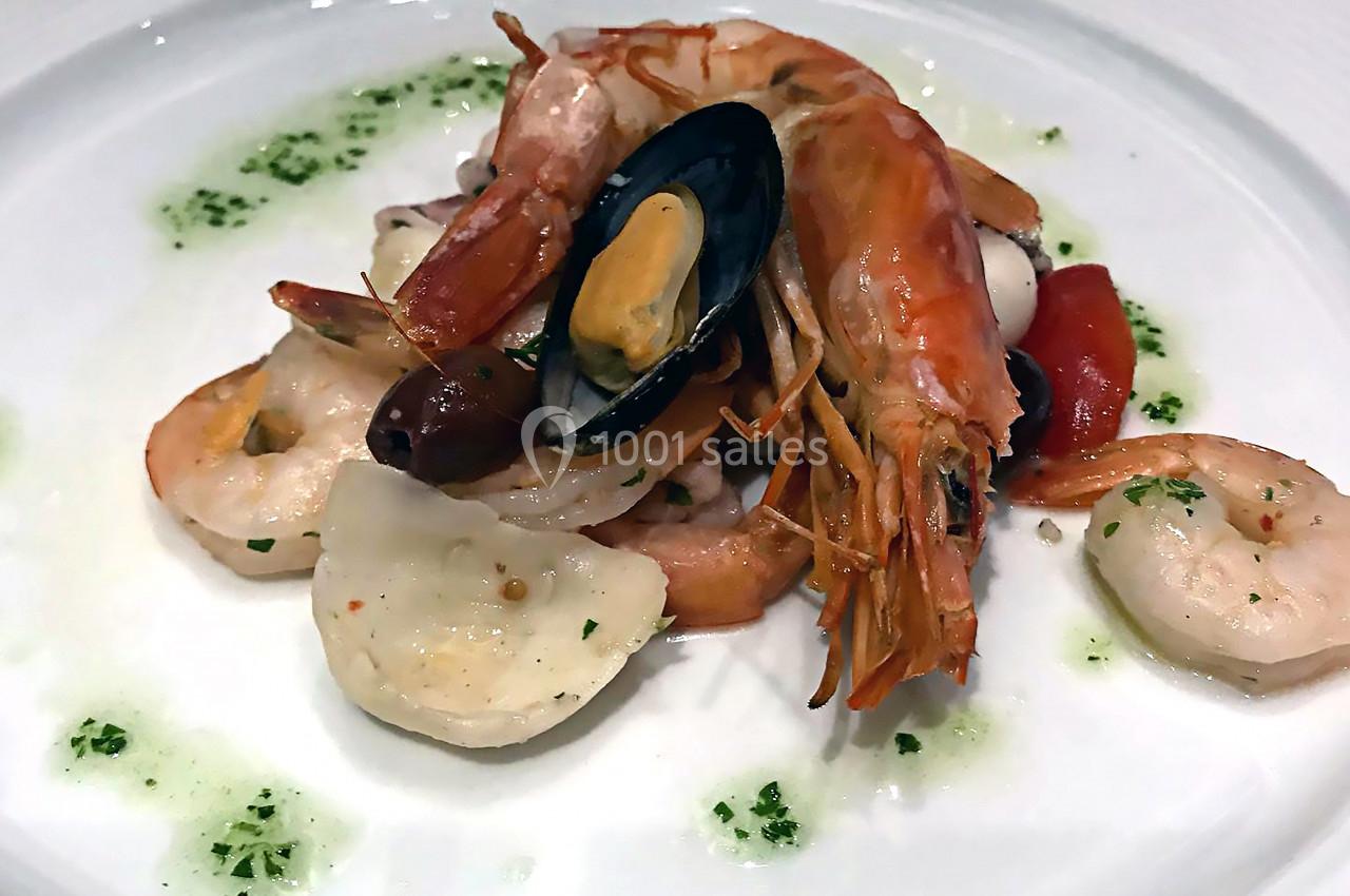 Assiette de fruits de mer avec crevettes, moules, calamars, tomates et herbes sur un lit de sauce verte.